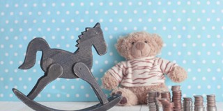 Een houten schommelpaard naast een teddybeer en stapels munten op een blauwe achtergrond met stippen.