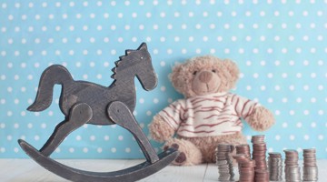 Een houten schommelpaard naast een teddybeer en stapels munten op een blauwe achtergrond met stippen.