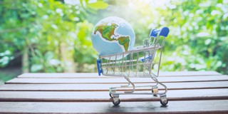 Een winkelwagentje met een globe erop, staat op een houten tafel in een groene, natuurlijke omgeving.