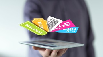 Een hand houdt een tablet vast waarop kortings- en ticketkaarten zweven met de teksten KORTING, TICKET en 50% KORTING.