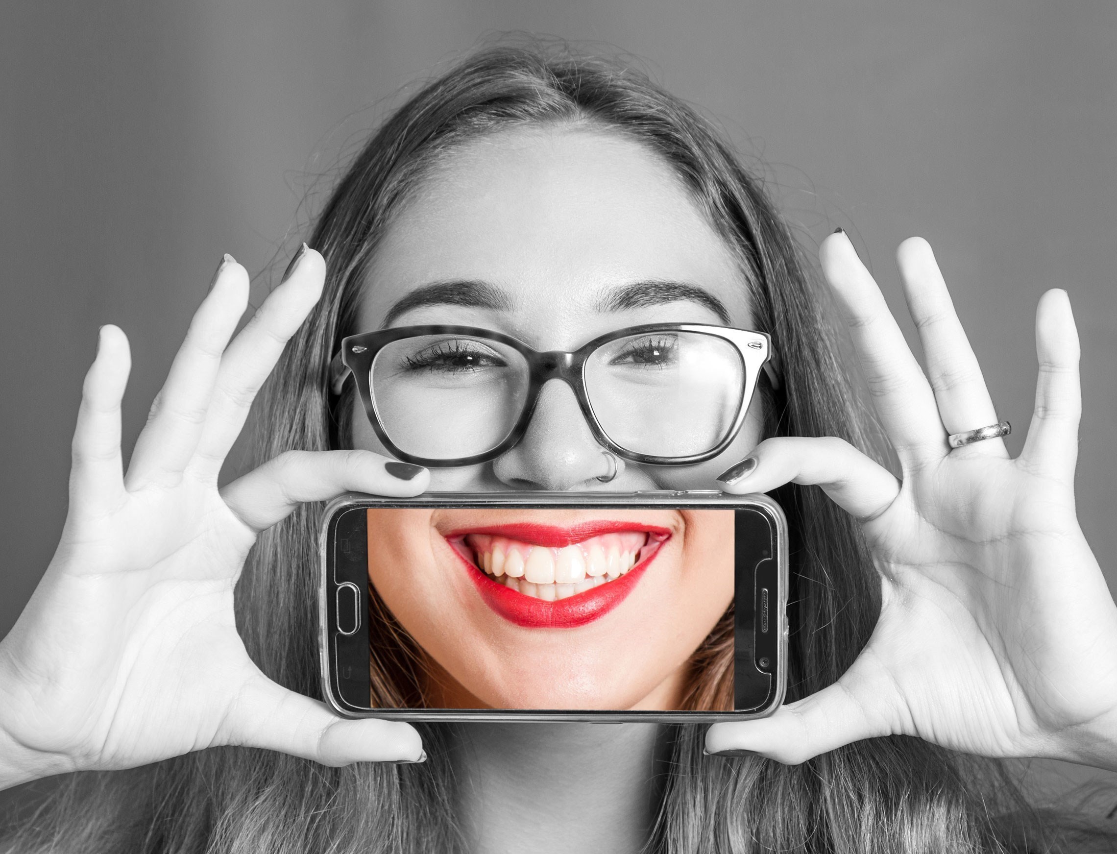 Een persoon houdt met beide handen een smartphone voor hun gezicht en kijkt naar de camera.