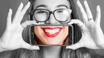 Een persoon houdt met beide handen een smartphone voor hun gezicht en kijkt naar de camera.