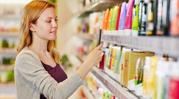 Vrouw maakt een foto met haar smartphone van verschillende verzorgingsproducten in een supermarkt.