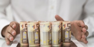 Vijf opgerolde briefjes van vijftig euro liggen in een rij, met handen aan de zijkanten die de nadruk op het geld leggen.