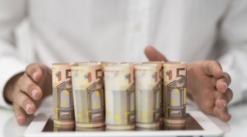 Vijf opgerolde briefjes van vijftig euro liggen in een rij, met handen aan de zijkanten die de nadruk op het geld leggen.