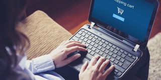 Persoon typt op een laptop terwijl een winkelwagentje met een blauwe achtergrond zichtbaar is.