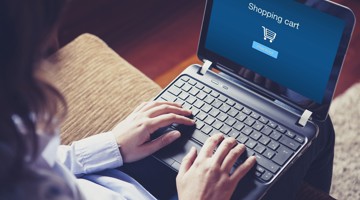 Persoon typt op een laptop terwijl een winkelwagentje met een blauwe achtergrond zichtbaar is.