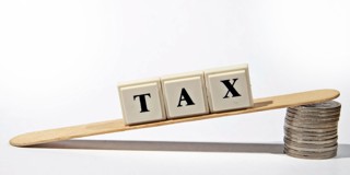 De blokletters TAX balans op een lepel, met aan de andere kant munten, wat de balans tussen belasting en financiën symboliseert.