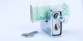 Een grijze geldkluis met een opgerold €100-biljet en een sleutel ernaast.