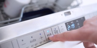Een hand drukt op de 'eco' knop van het bedieningspaneel van een vaatwasser.