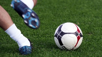 Een voet raakt een voetbal op een groene grasmat.