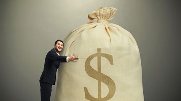 Een man in zwart pak omarmt een grote zak met een dollar-teken, wat financieel succes of rijkdom symboliseert.