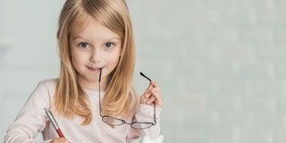 Meisje met lang, blond haar houdt een pen en een bril vast terwijl ze op een notitieblok schrijft.