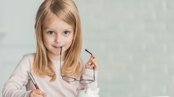 Meisje met lang, blond haar houdt een pen en een bril vast terwijl ze op een notitieblok schrijft.
