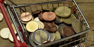 Een winkelwagentje vol met een mix van euro-munten, geplaatst op een houten ondergrond.