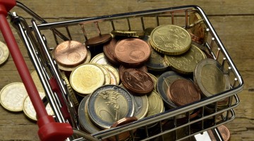 Een winkelwagentje vol met een mix van euro-munten, geplaatst op een houten ondergrond.