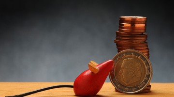 Een rode rubberen stop met een houten kurk ligt naast een stapel munten en een euromunt, wat besparingen en geldbeheer symboliseert.