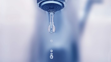 Een druppel water valt van een kraan met een onscherpe achtergrond.