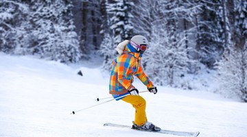 Skiër in kleurrijke outfit glijdt over een besneeuwd berglandschap.