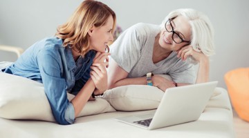Twee personen zitten op een bank en kijken samen naar een laptop in een sfeervolle woonkamer.