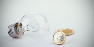 Gloeilamp naast twee munten van twee euro, symboliseert energie- en kostenbesparing.