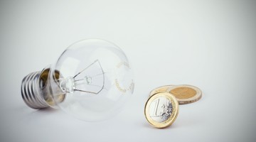 Gloeilamp naast twee munten van twee euro, symboliseert energie- en kostenbesparing.