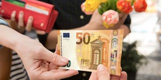 Een hand overhandigt een vijftig eurobiljet aan een andere hand, terwijl iemand bloemen vasthoudt.