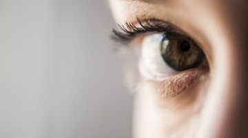 Nabijbeeld van een oog met een heldere groene iris en lange wimpers, volledig gericht op de pupil.