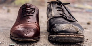 Vergelijking van een nieuwe, glanzende bruine schoen naast een versleten, beschadigde zwarte schoen op een ruwe ondergrond.