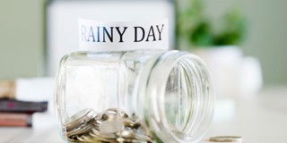 Glazen pot met munten en een label met de tekst RAINY DAY, als symbool voor een spaarpot voor noodgevallen.