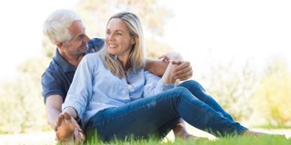 Een stel zit ontspannen in het gras, de man omarmt lachend de vrouw van achteren terwijl ze samen van het moment genieten.