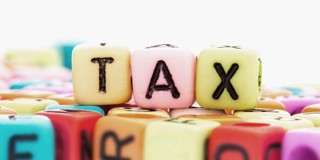 Verkleure blokken met de letters 'TAX' in het midden, omgeven door andere speelse letterblokjes.