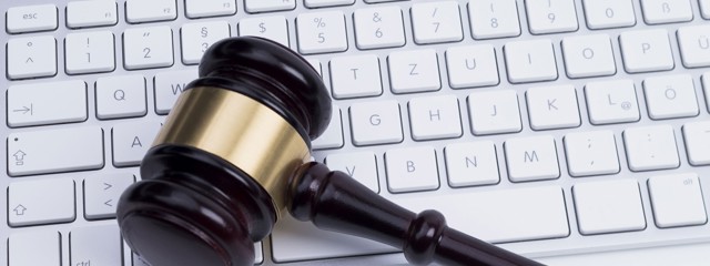 Een houten hamer ligt op een wit computerkeyboard, wat de verbinding tussen recht en technologie symboliseert.