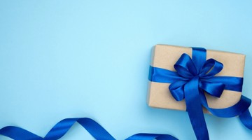 Cadeau verpakt in bruin papier met een blauwe strik op een lichtblauwe achtergrond.