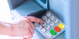 Une main appuie sur le clavier d'un distributeur automatique de billets, avec des chiffres et des fonctions, y compris un bouton vert et un bouton jaune.