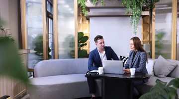 Een man en een vrouw werken samen aan een laptop aan een ronde tafel in een moderne kantoorruimte met planten.