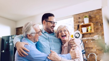 Drie mensen omarmen elkaar in een lichte, moderne keuken met houten details.