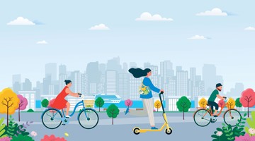 Vrouwen op een fiets en een step, met kinderen op fietsen achter hen, terwijl op de achtergrond een stad zichtbaar is. Groene en kleurrijke bomen in een park.