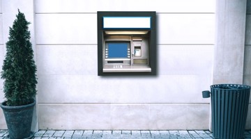 Een geldautomaat tegen een muur, met een leeg scherm en aan weerszijden een paar planten.