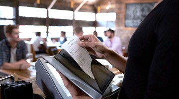 Une main tient un bon pendant qu'il est scanné à une caisse en libre-service dans un restaurant.