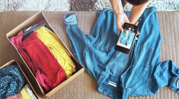 Une personne prend une photo d'une chemise en denim tandis qu'une boîte de vêtements colorés est posée à côté.
