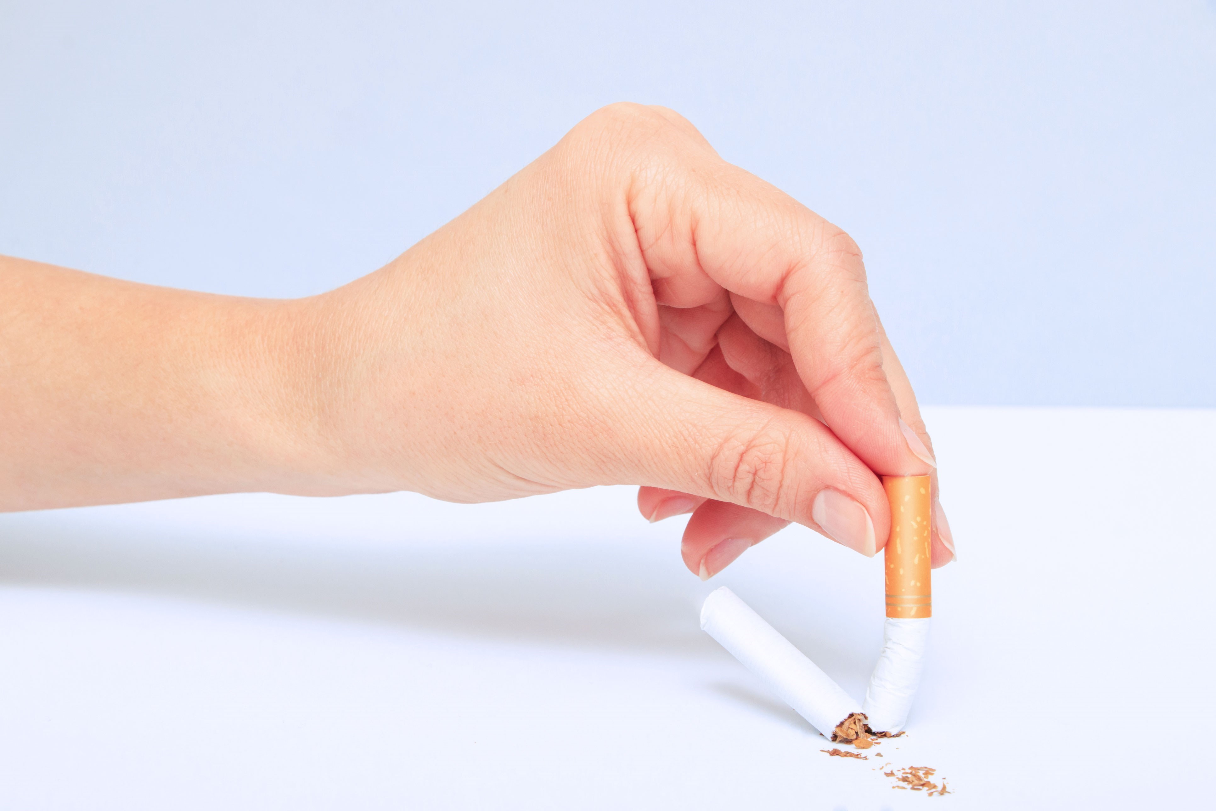 Een hand houdt een sigaret vast, klaar om deze uit te drukken op een tafel bedekt met tabakskruimels.