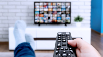 Personne assise sur le canapé avec une télécommande à la main, regardant la télévision affichant un collage d'images.