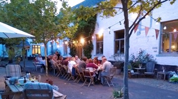 Groupe de personnes dînant à une longue table en extérieur, entourées de lumières et d'arbres.