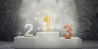 Un podium avec trois chiffres : un '1' doré au centre et un '2' et '3' orange de chaque côté, éclairés par un projecteur.
