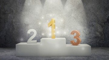 Un podium avec trois chiffres : un '1' doré au centre et un '2' et '3' orange de chaque côté, éclairés par un projecteur.