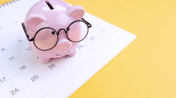 Cochon tirelire rose avec des lunettes, placé sur un calendrier avec la date visible, symbolise l'épargne et la planification financière.