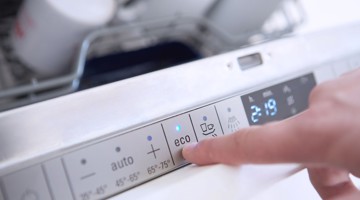 Une main pointe vers le bouton éco sur le panneau de contrôle d'un lave-vaisselle.