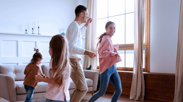 Une famille danse joyeusement dans le salon, avec de grandes fenêtres laissant entrer la lumière naturelle.
