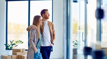 Deux personnes dans un environnement de bureau moderne, s'enlaçant, avec des cartons de déménagement en arrière-plan et de la lumière naturelle qui entre.